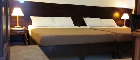 Uma cama de casal com duas almofadas, uma mesa de cabeceira com abajur e uma cadeira.