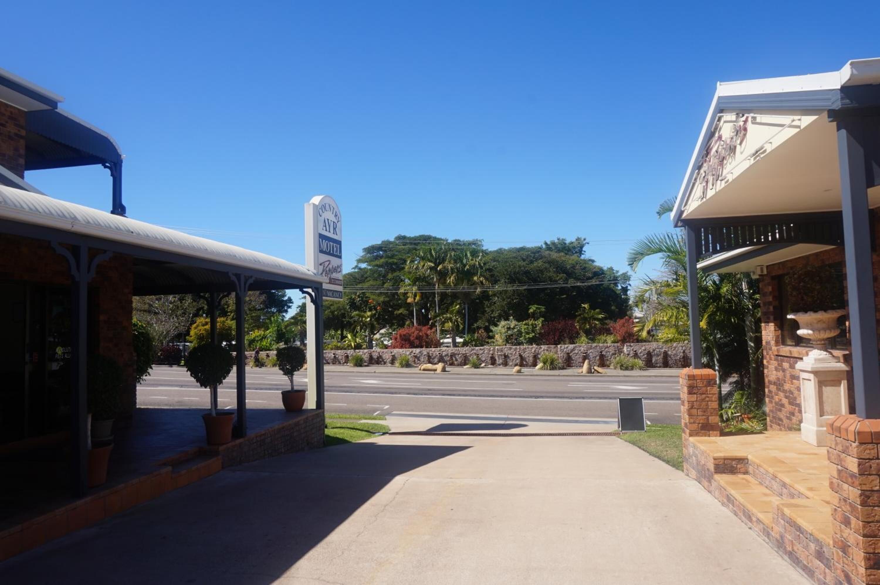 A motel with a covered parking area, a signboard, and a landscaped garden.