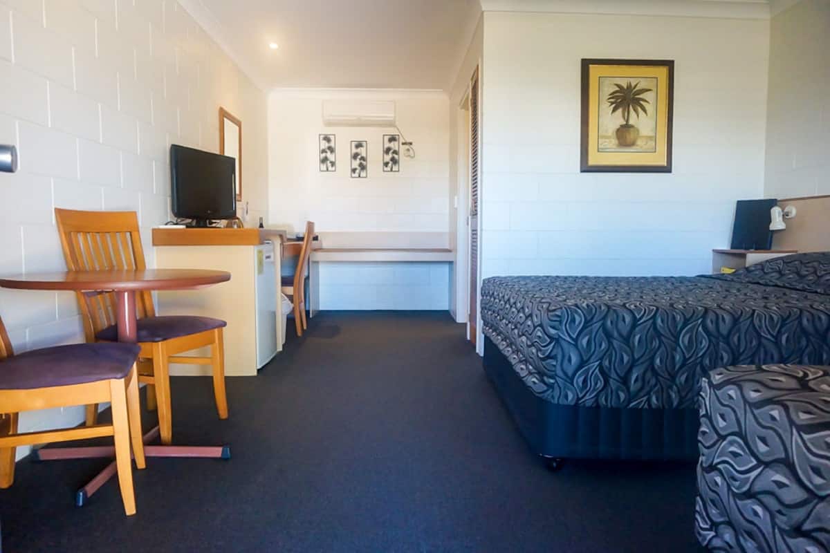 Habitación de hotel con cama, escritorio con silla, televisión y un cuadro en la pared.