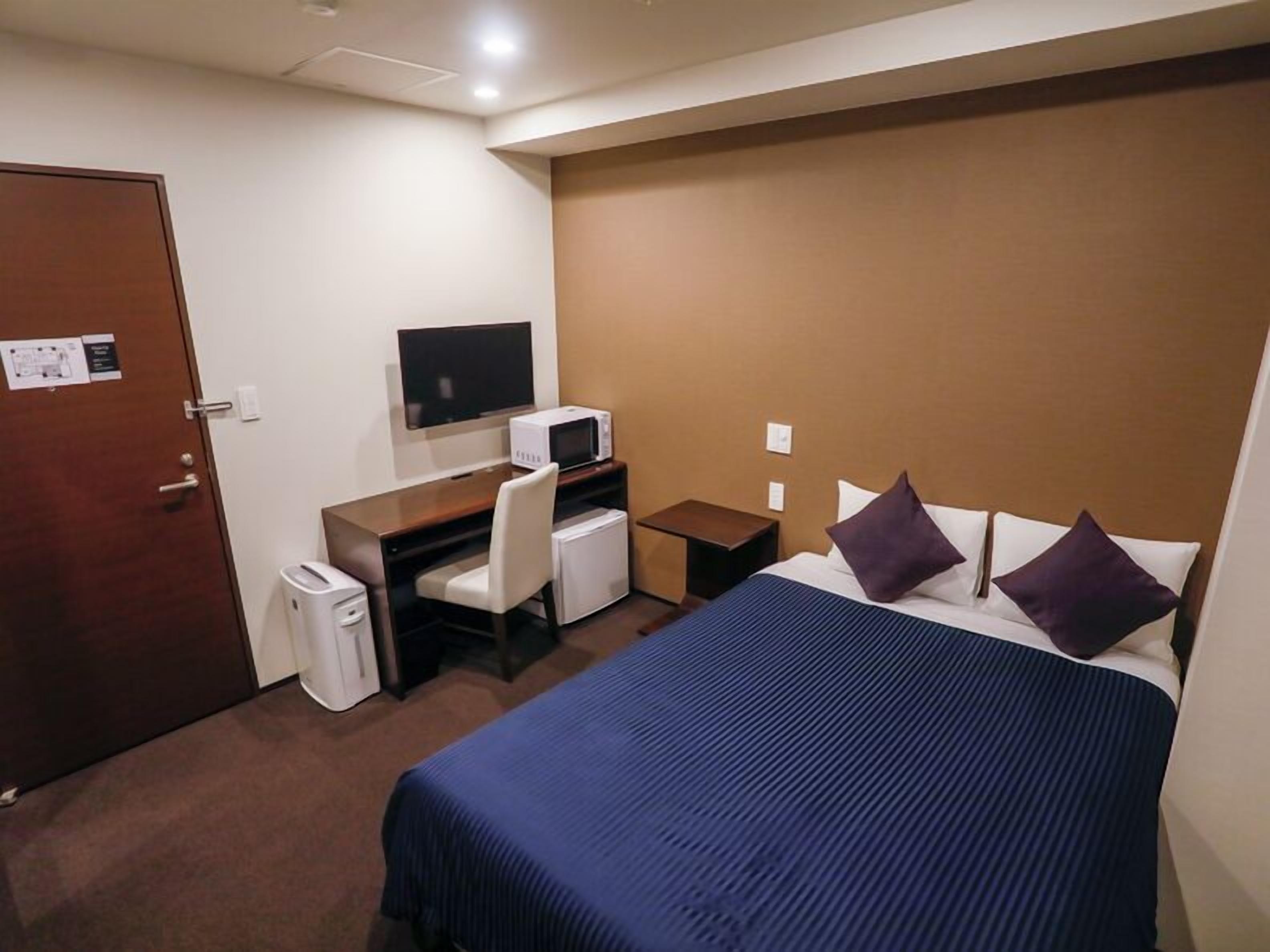 A hotel room with a bed, a desk with a chair, a television, and a microwave.