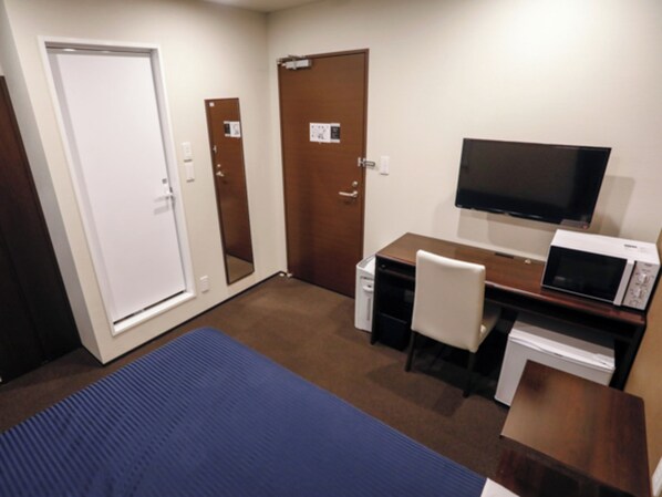Una habitación de hotel con una cama, un escritorio, una silla, un televisor y un microondas.