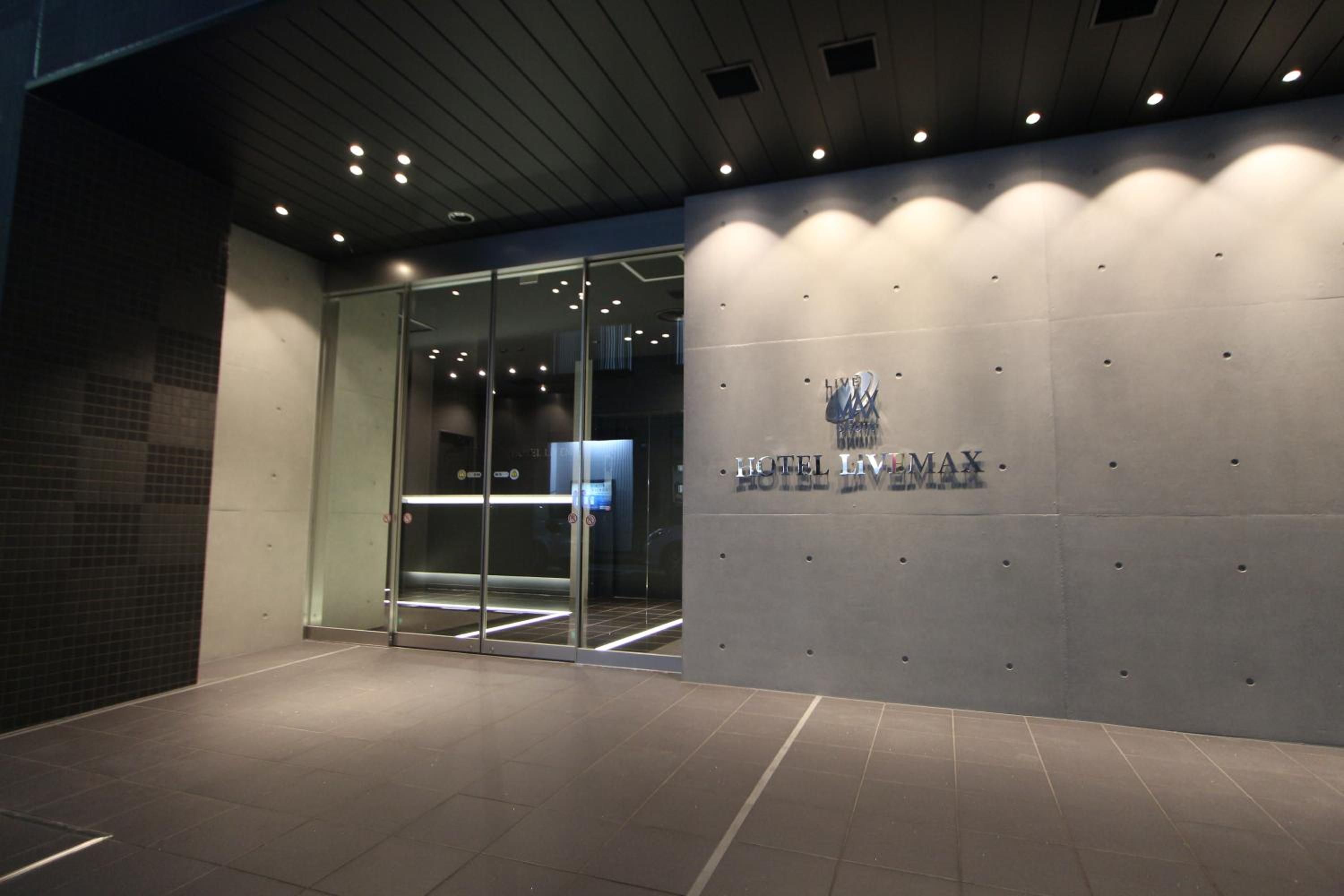 A modern hotel entrance with a glass door, a tiled floor, and a wall with the hotel's name.