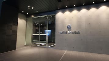 A modern hotel entrance with a glass door, a tiled floor, and a wall with the hotel's name.