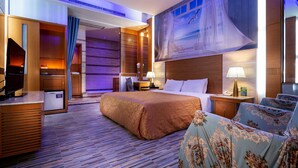 Habitación de hotel con una cama grande, un escritorio con computadora, un televisor y un ventanal con vista a la ciudad.