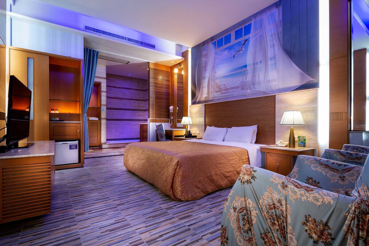 A hotel room with a large bed, a desk with a computer, a TV, and a large window with a view of the city.