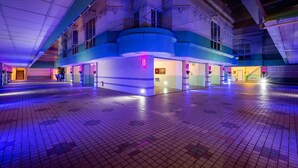 Un amplio y moderno atrio con techo alto y una estructura central iluminada en azul, posiblemente un vestíbulo o área pública.