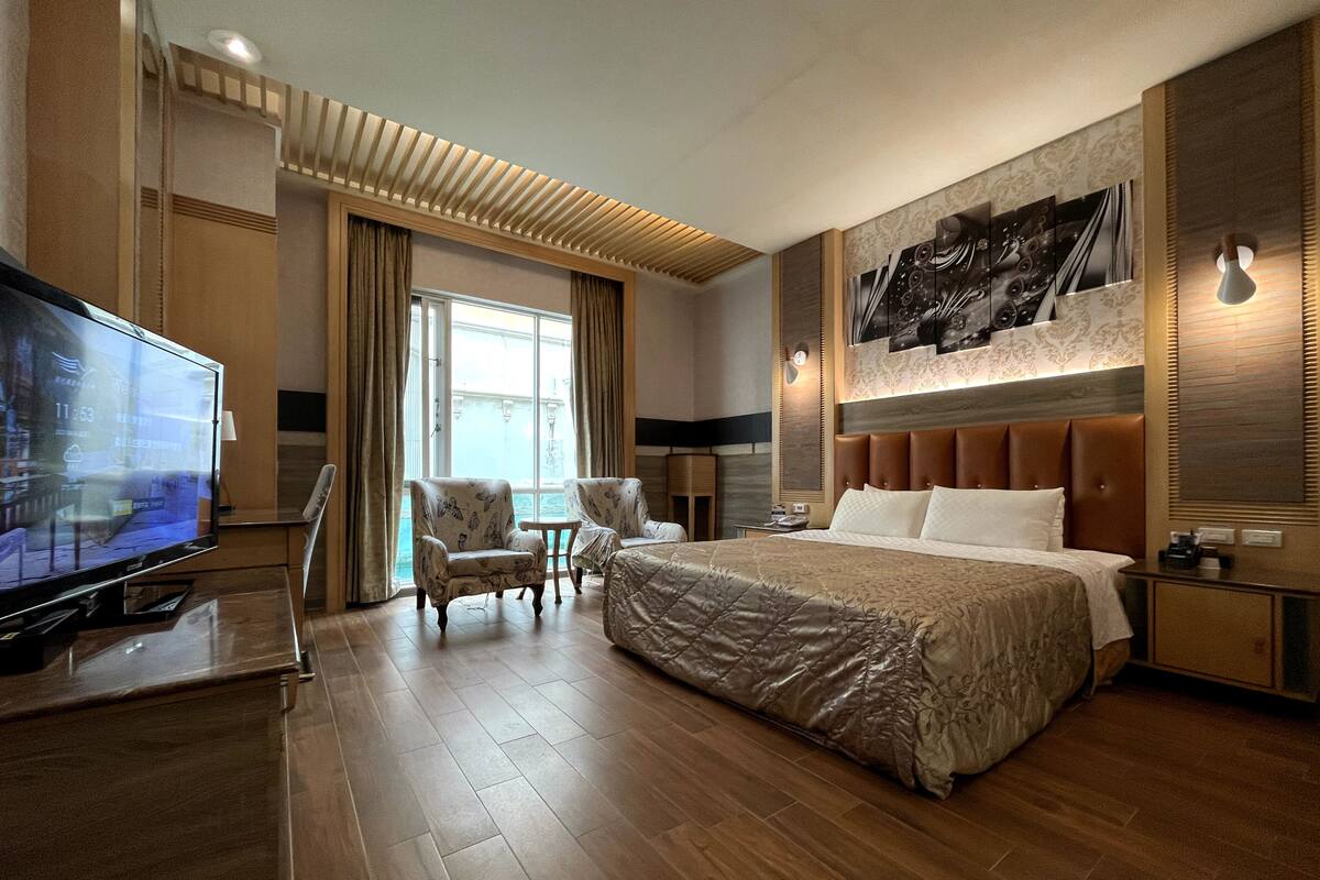 A hotel room with a large bed, a television, a desk, and a chair.