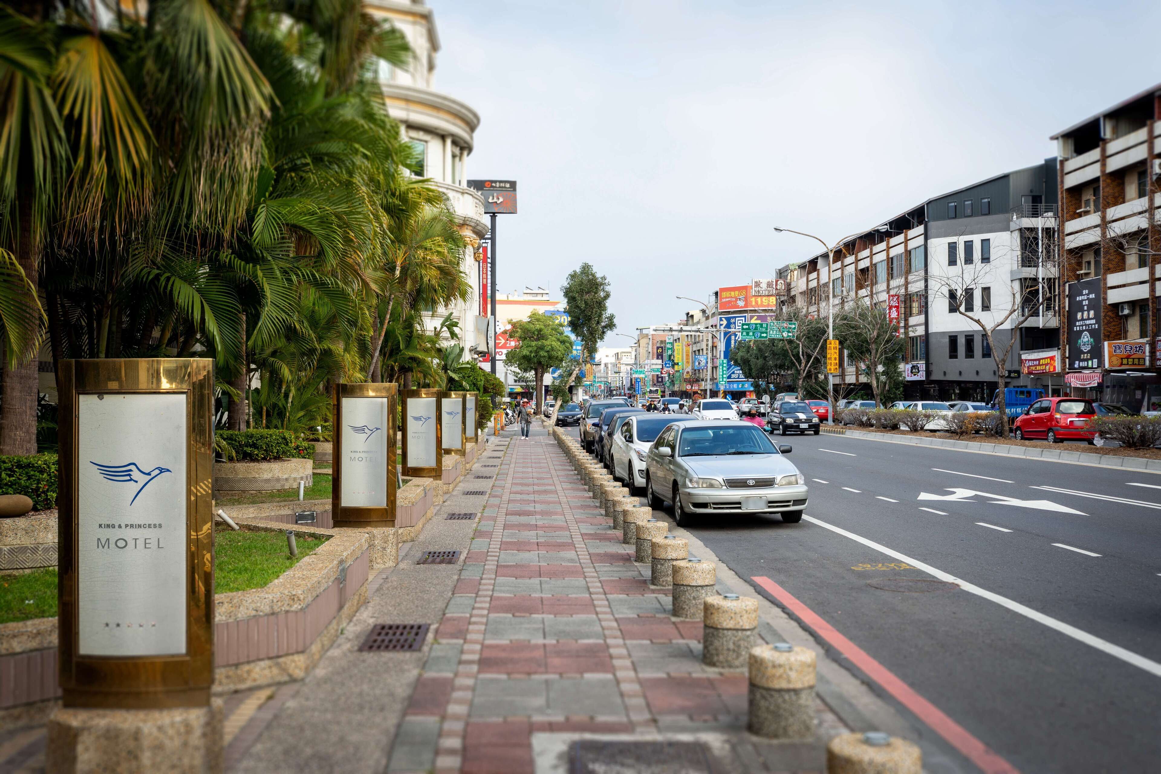 A street view with a row of parked cars, a sidewalk with bollards, and a building with a sign for a motel.