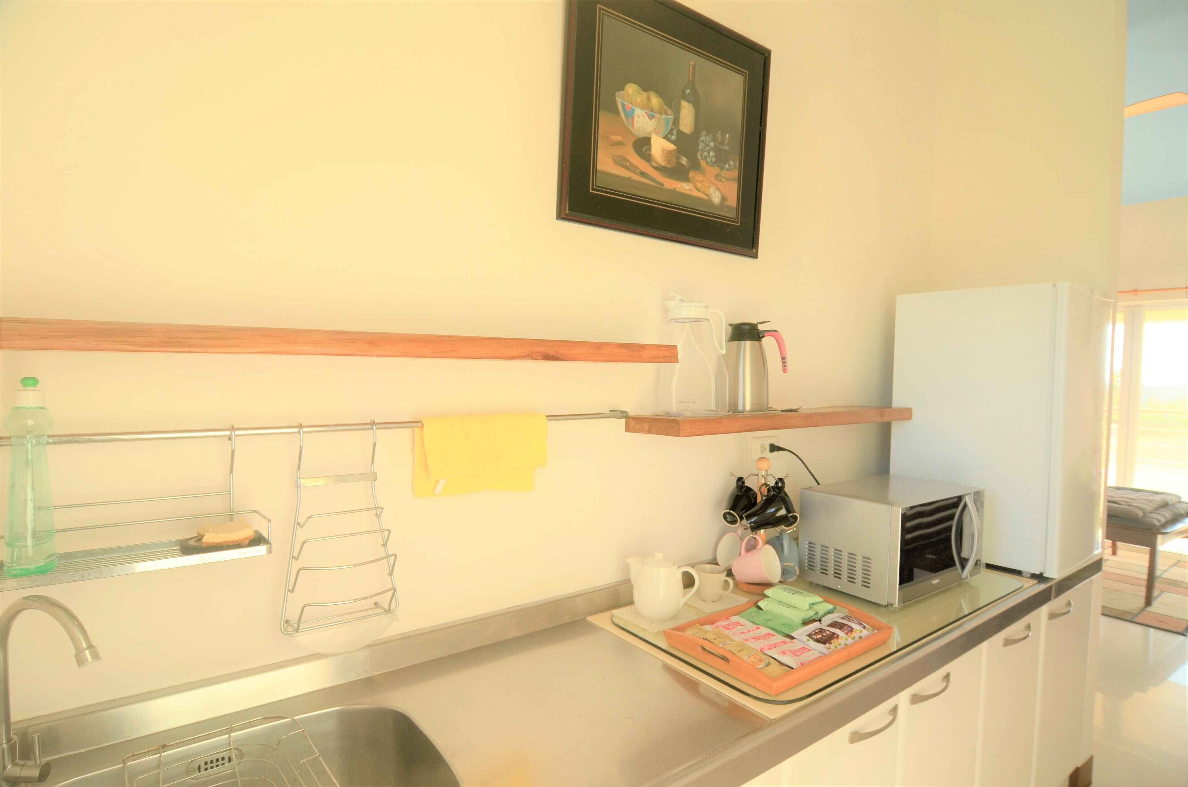 A kitchen with a sink, a microwave, a kettle, and a shelf with various items.