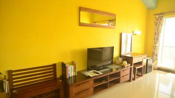 Una habitación con un banco de madera, un televisor de pantalla plana, una pequeña mesa con libros, un espejo y una ventana con cortinas.