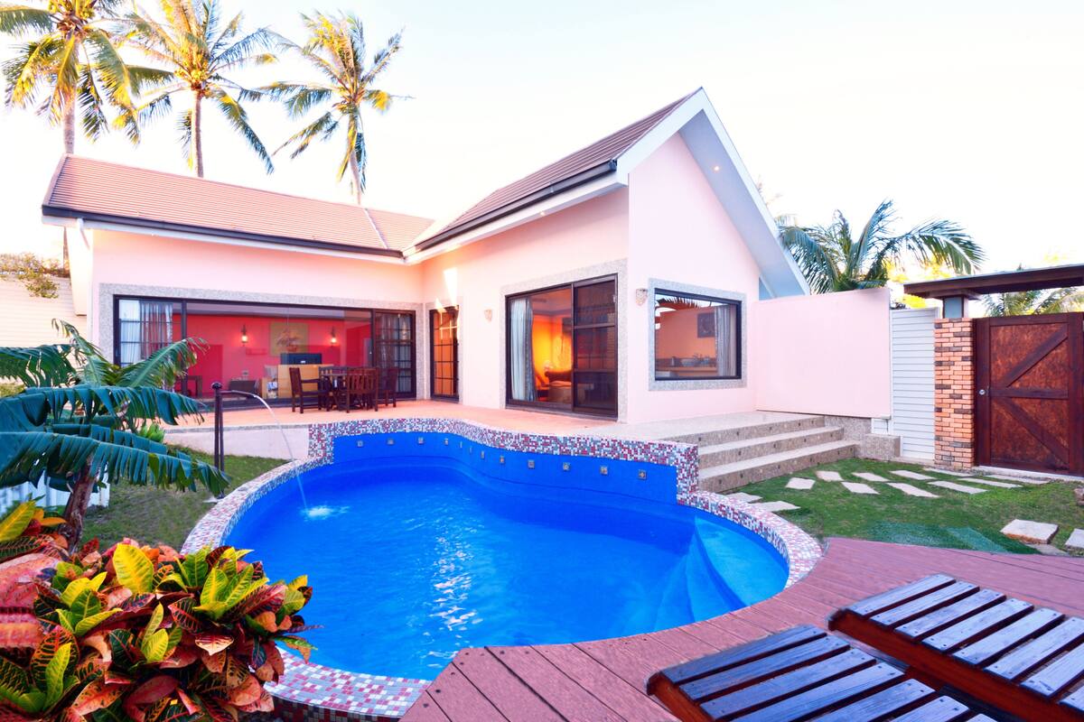 A modern house with a swimming pool, a patio with wooden loungers, and a well-maintained garden.