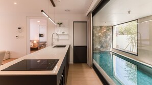Una cocina moderna con una isla central, un comedor con mesa y sillas, y vista a una piscina a través de un muro de vidrio.