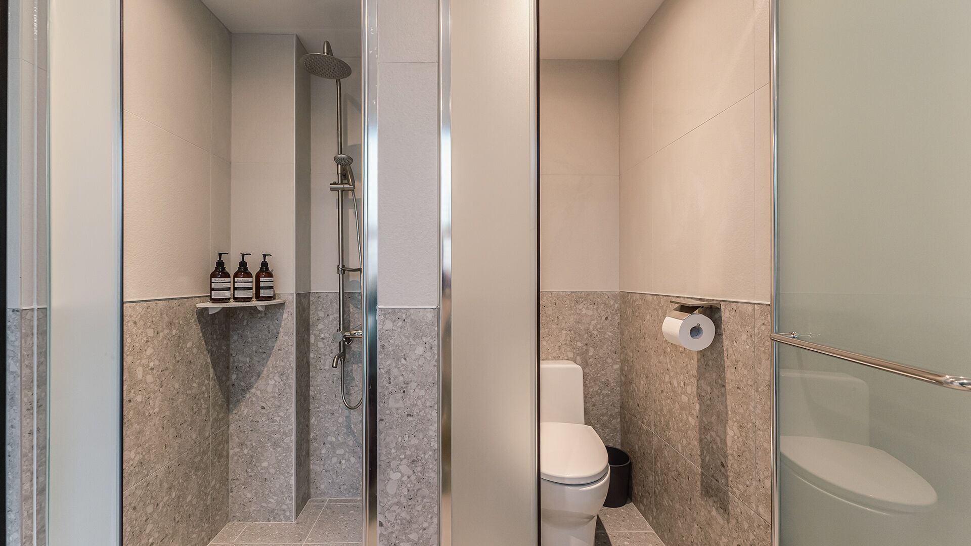 A modern bathroom with a glass-enclosed shower, a toilet, and a shelf with toiletries.