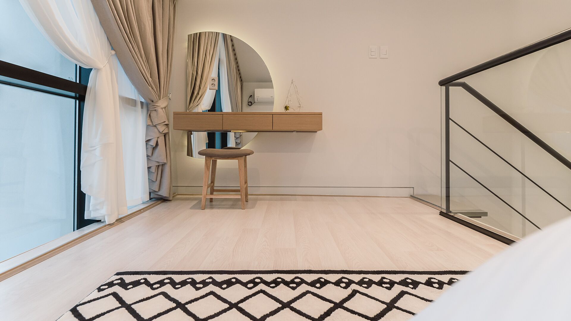 Un dormitorio moderno con un escritorio de madera, una silla, un espejo grande y una alfombra estampada.