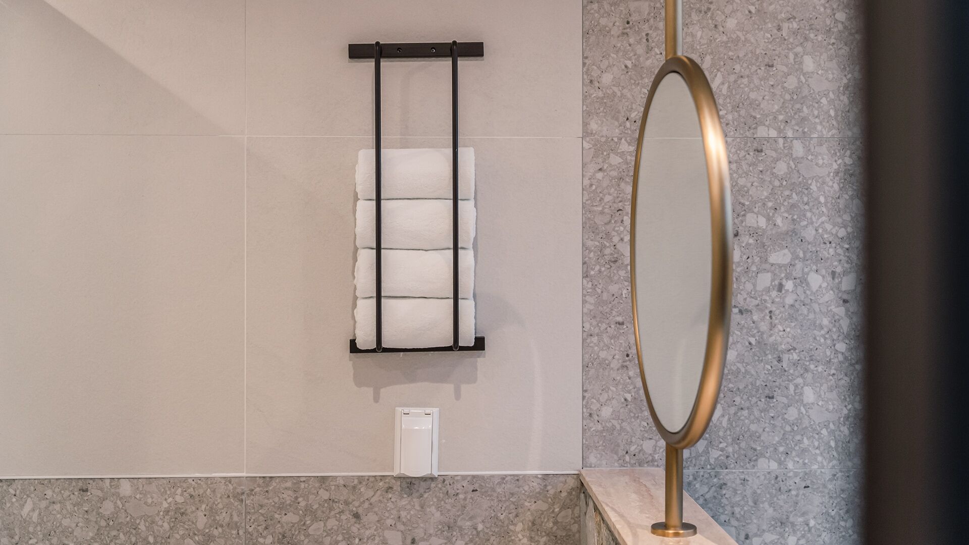Een badkamer met een handdoekrek vol handdoeken, een spiegel met gouden lijst, en een marmeren vloer.