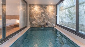 A spa room with a stone wall, a hot tub, and a bed. - Albescent Pool Villa (Gyeongju)