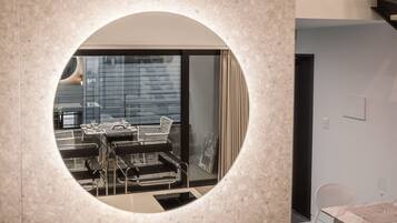 A circular mirror reflecting a dining area with a table and chairs, a window with blinds, and a door leading to another room.