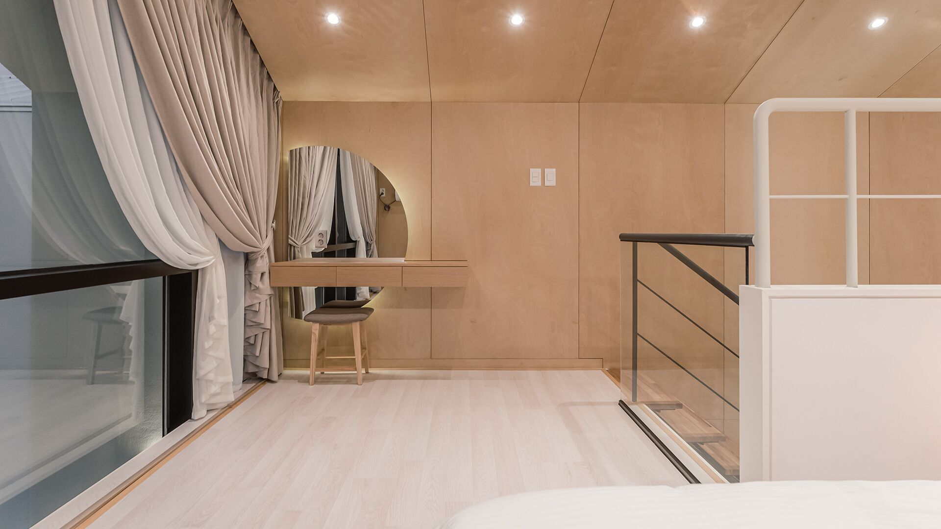 A modern bedroom with a wooden floor, a desk with a chair, a bed, and a window with curtains.