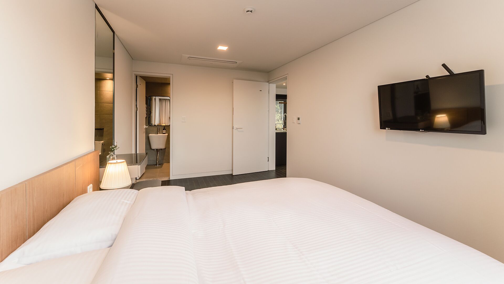 A hotel room with a large bed, a TV mounted on the wall, and a bathroom visible through an open door.