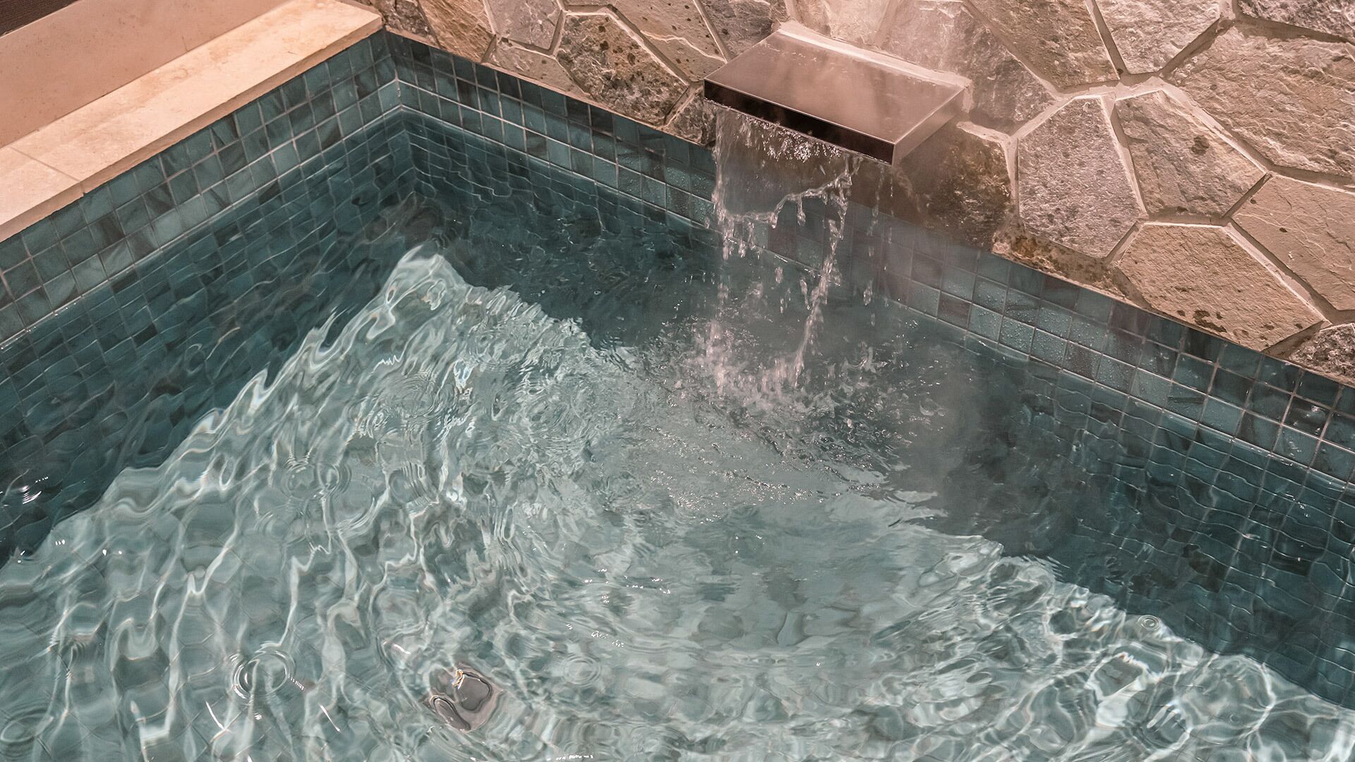 Piscina cristalina con agua que se desliza por el borde, rodeada de baldosas de piedra.