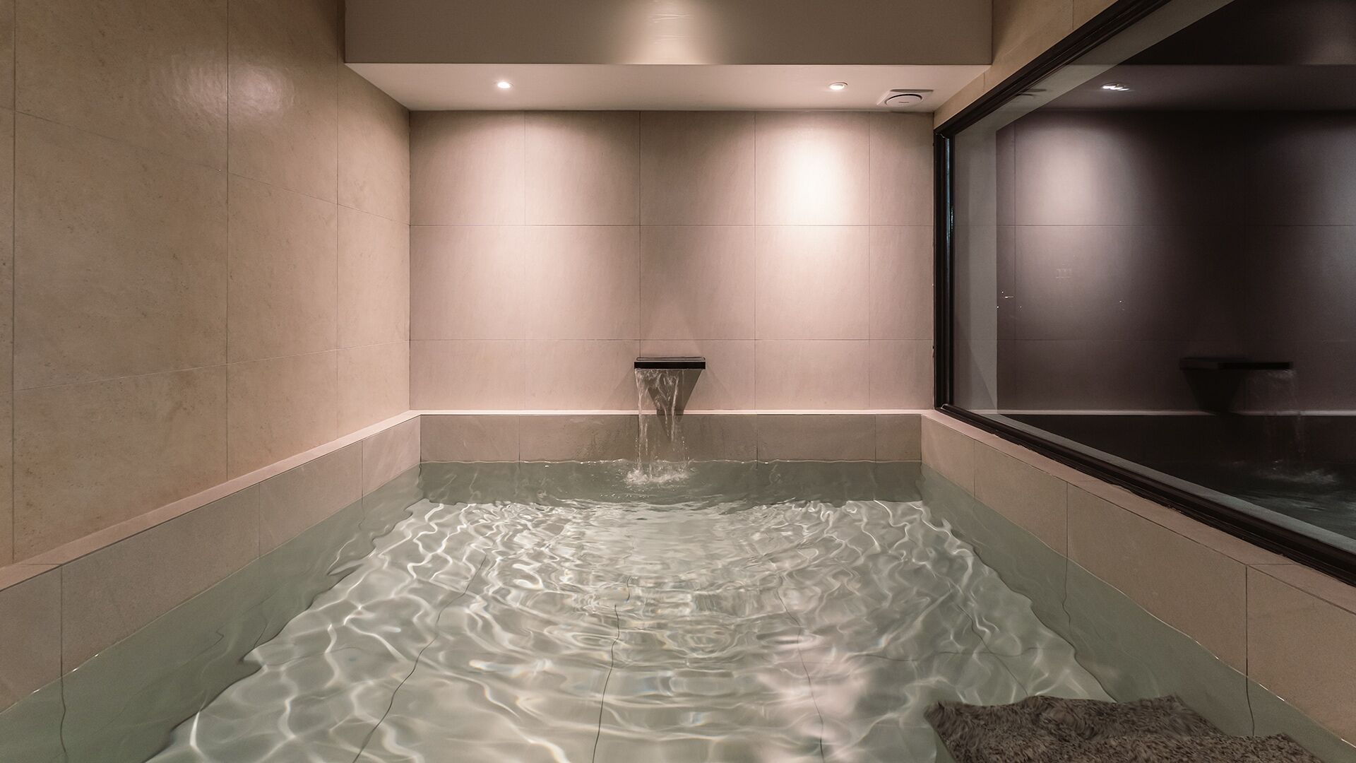 Une salle de bain moderne dotée d’une douche à parois de verre, d’un jet d’eau visible et d’une fenêtre offrant une vue sur l’extérieur.