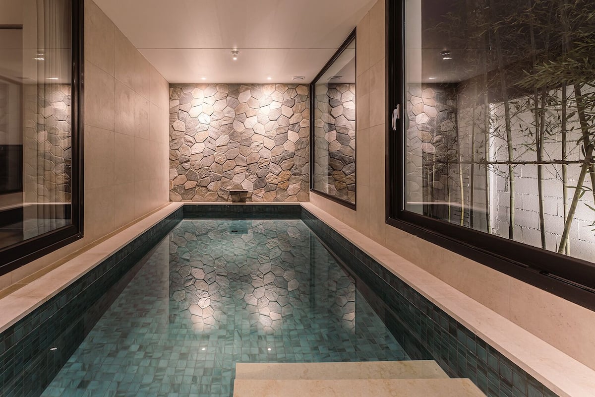 A narrow indoor pool with stone walls and glass panels.