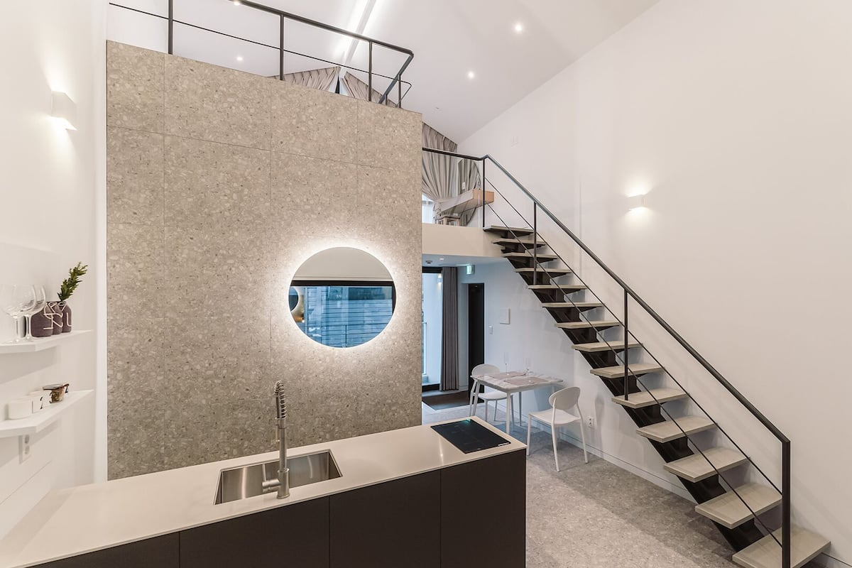 A modern kitchen with a central island, a round window, and a staircase leading to an upper level.
