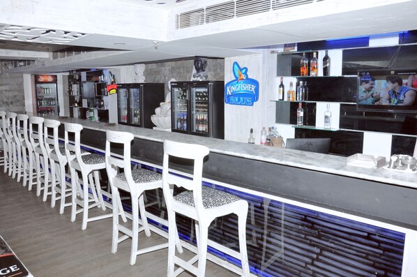 A bar area with white bar stools, a counter, and shelves with bottles.