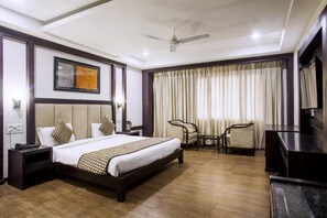 A hotel room with a bed, bedside tables, a TV, a ceiling fan, and a large window with curtains.