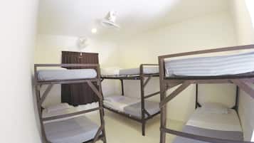 A dormitory room with bunk beds, a ceiling fan, and a window with curtains.