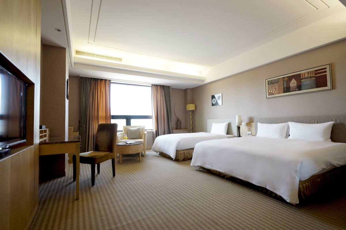 Habitación de hotel con dos camas, un escritorio, una silla, un televisor y una ventana con cortinas.