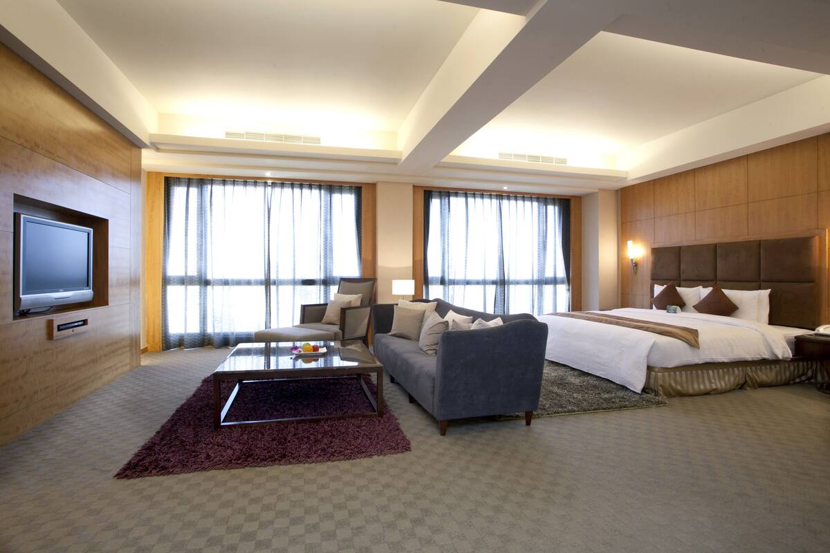 Una habitación de hotel con una cama grande, un sofá, una mesa de centro y un televisor.
