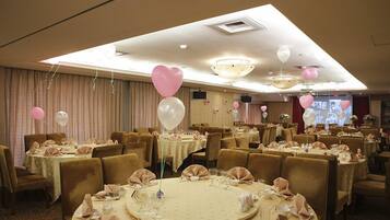 A banquet hall with round tables set for dining, featuring a warm color scheme and elegant decor.
