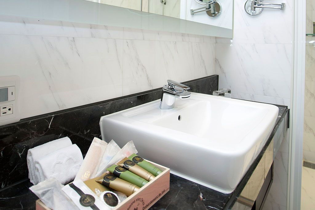 A bathroom with a white sink, black countertop, and marble backsplash. There is a box of toiletries on the countertop.