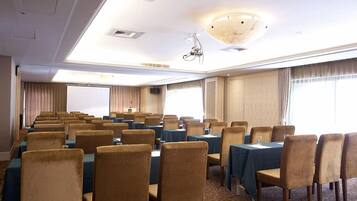 A conference room with rows of tables and chairs, large windows, and a projector screen.