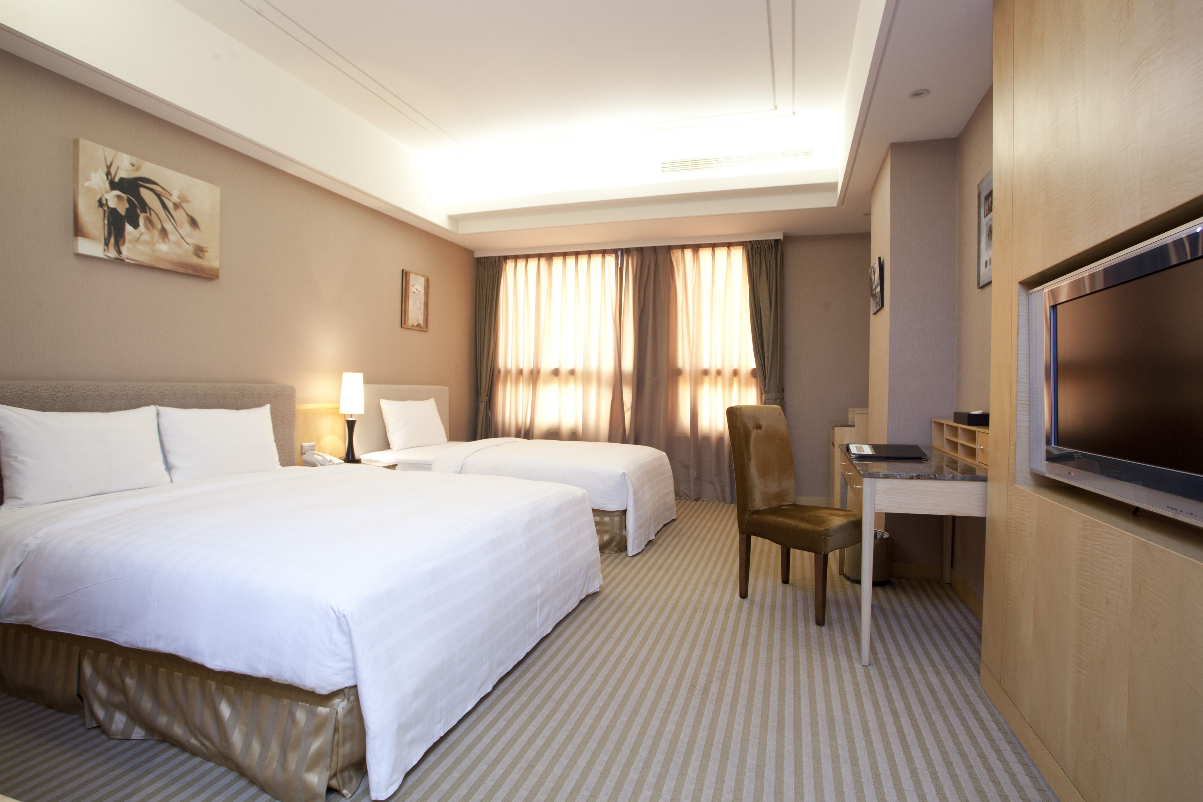 Une chambre d’hôtel avec deux lits, un bureau, une chaise, une télévision et une fenêtre avec des rideaux.