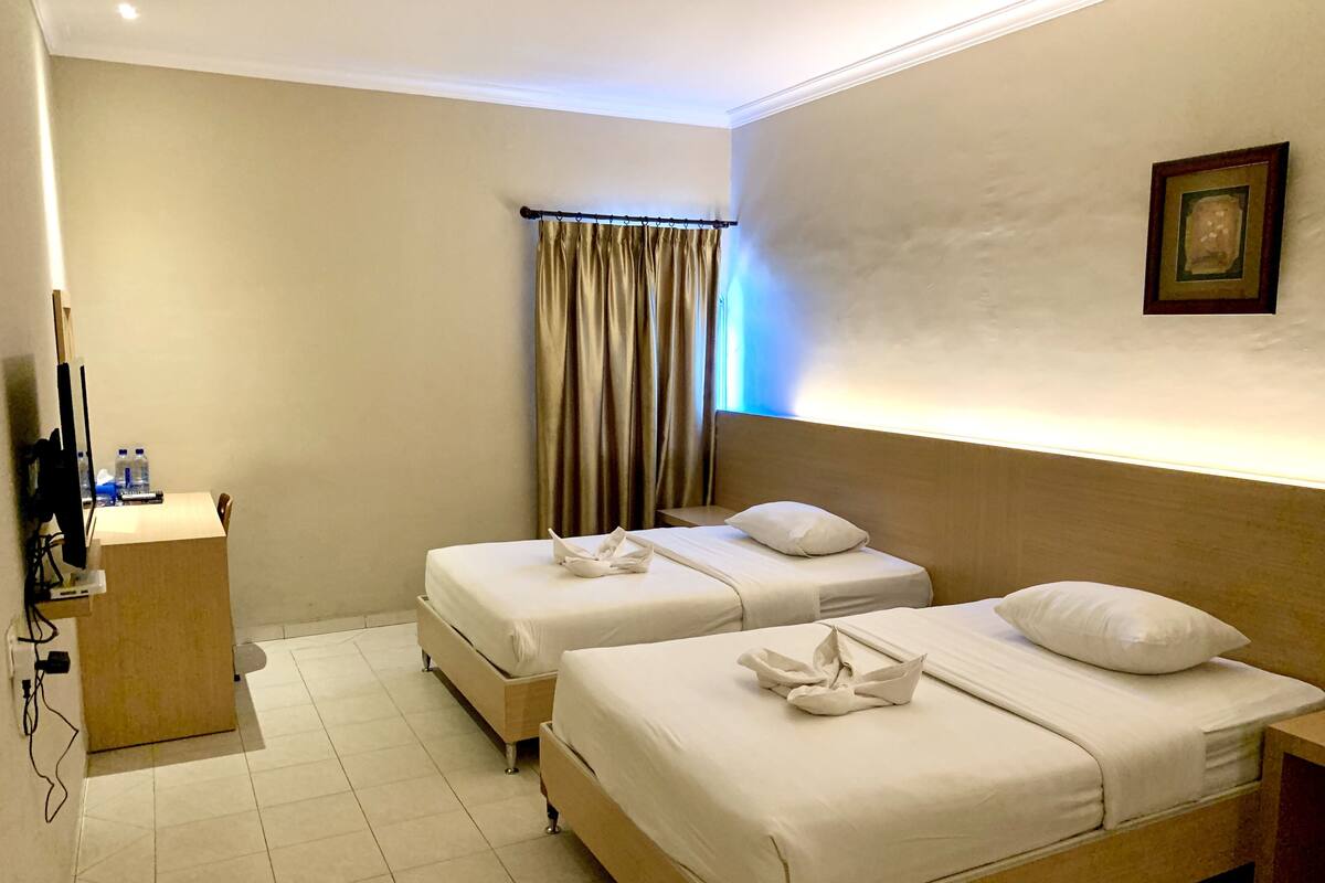 Une chambre d’hôtel avec deux lits, un bureau, une télévision et un rideau.