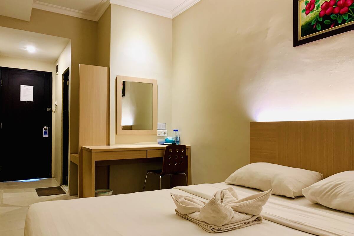 Une chambre d’hôtel avec un lit, un bureau, une chaise, un miroir et une porte.