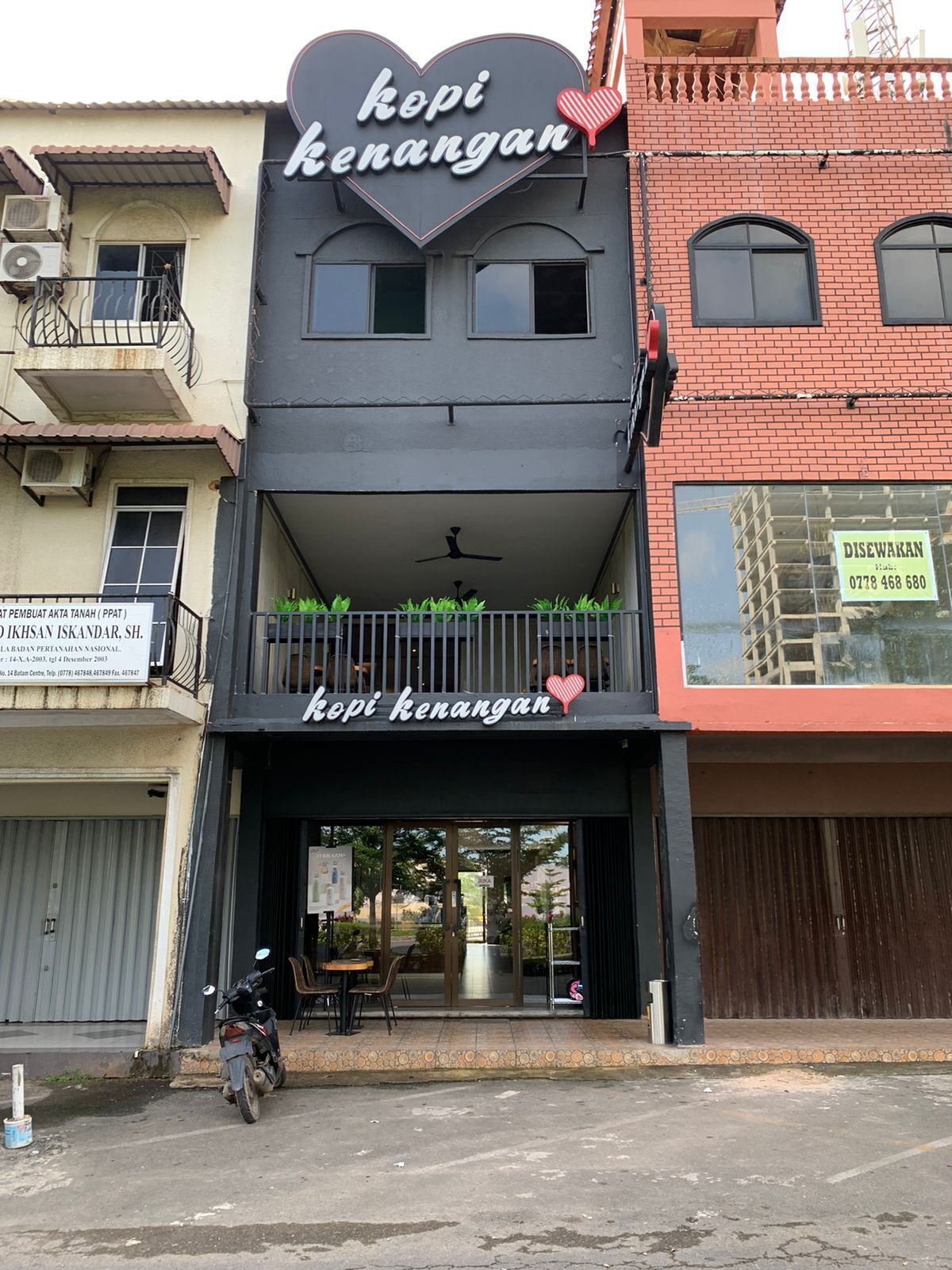 Un edificio con un letrero en forma de corazón que dice "kopi kenangan" y un balcón con sillas y mesas.