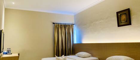 Habitación de hotel con dos camas, un escritorio con silla, una cortina y un cuadro en la pared.