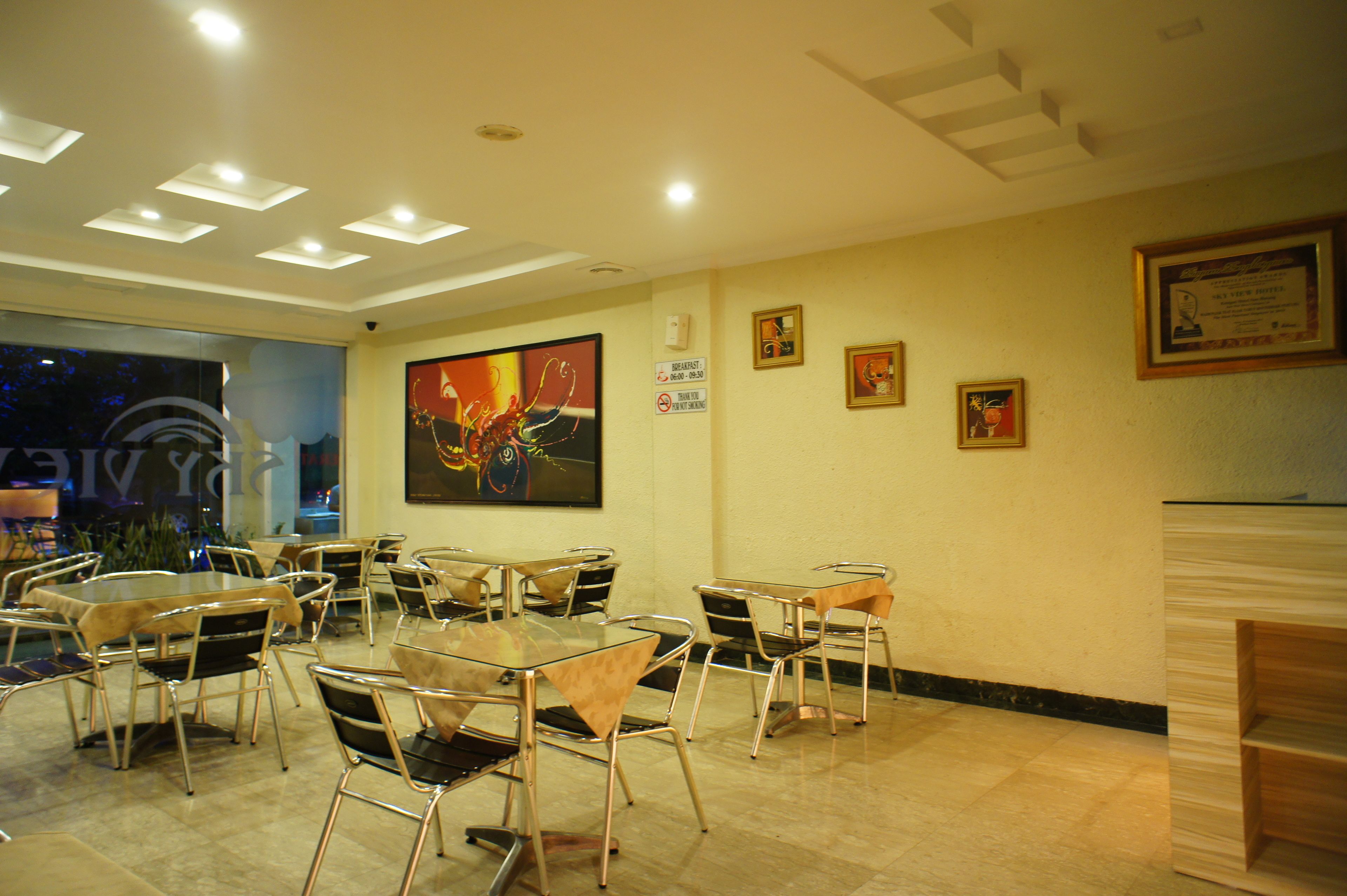 Un restaurant au décor moderne, avec des tables en verre et des chaises en métal, une grande peinture abstraite au mur et des tableaux encadrés.