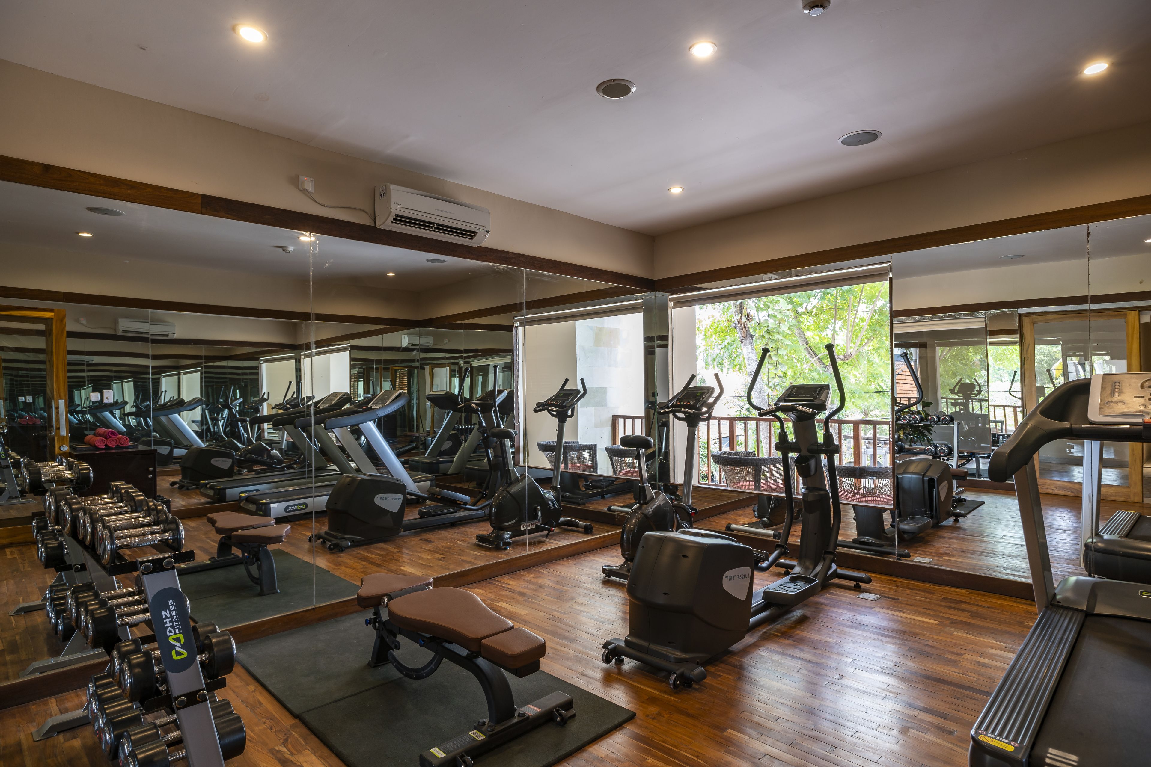 A gym with various exercise equipment, mirrors, and a wooden floor.
