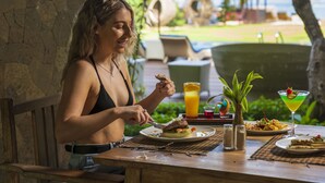 A person dining at an outdoor table with a meal, a drink, and a tropical plant. - d’Nusa Beach Club and Resort (Lembongan Island)
