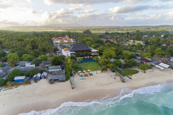 An aerial view of a coastal resort with beachside villas, a pool area, and a beach with umbrellas. - d’Nusa Beach Club and Resort (Lembongan Island)