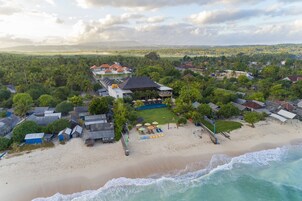 Vista aérea de um resort costeiro com vilas à beira-mar, área de piscina e uma praia com guarda-sóis.