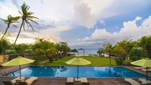 A wooden deck with lounge chairs and umbrellas, a swimming pool, palm trees, and a view of the sea. - d’Nusa Beach Club and Resort (Lembongan Island)