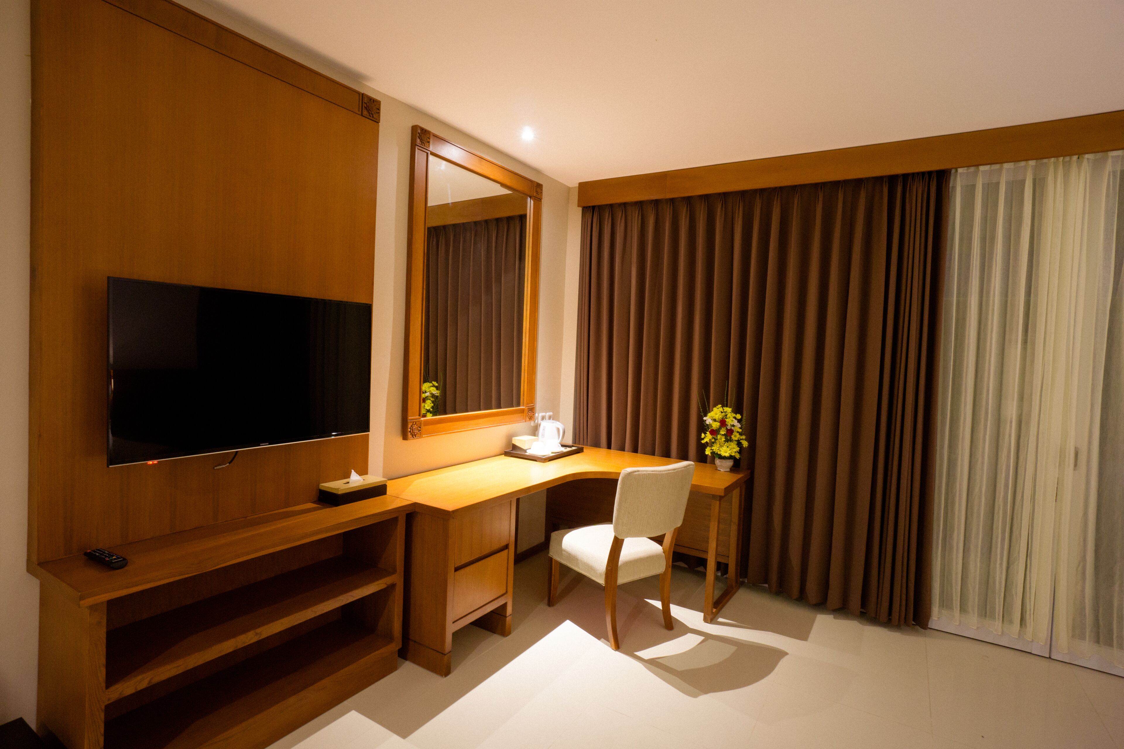 Hotelkamer met een houten bureau, een televisie, een stoel en een groot raam met gordijnen.