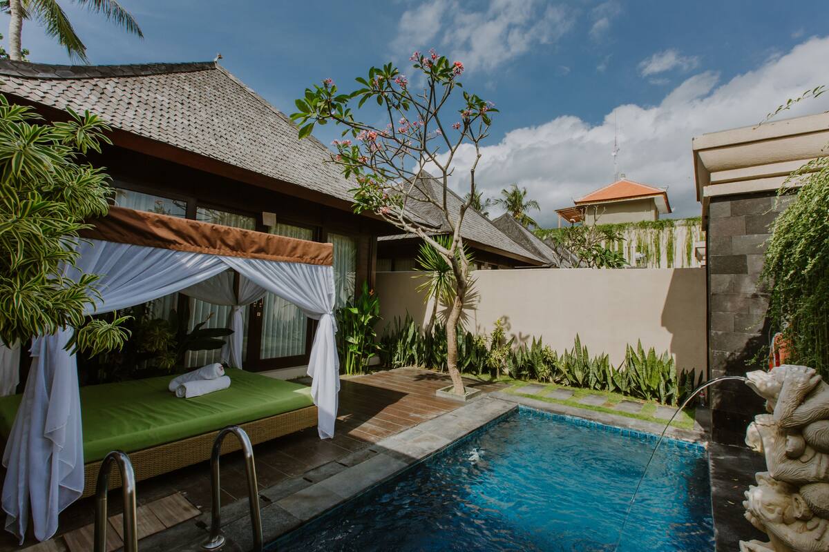 A poolside area with a bed, a small tree, and a stone wall.