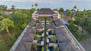 A resort with multiple thatched-roof villas, a central pool, and a view of the ocean.