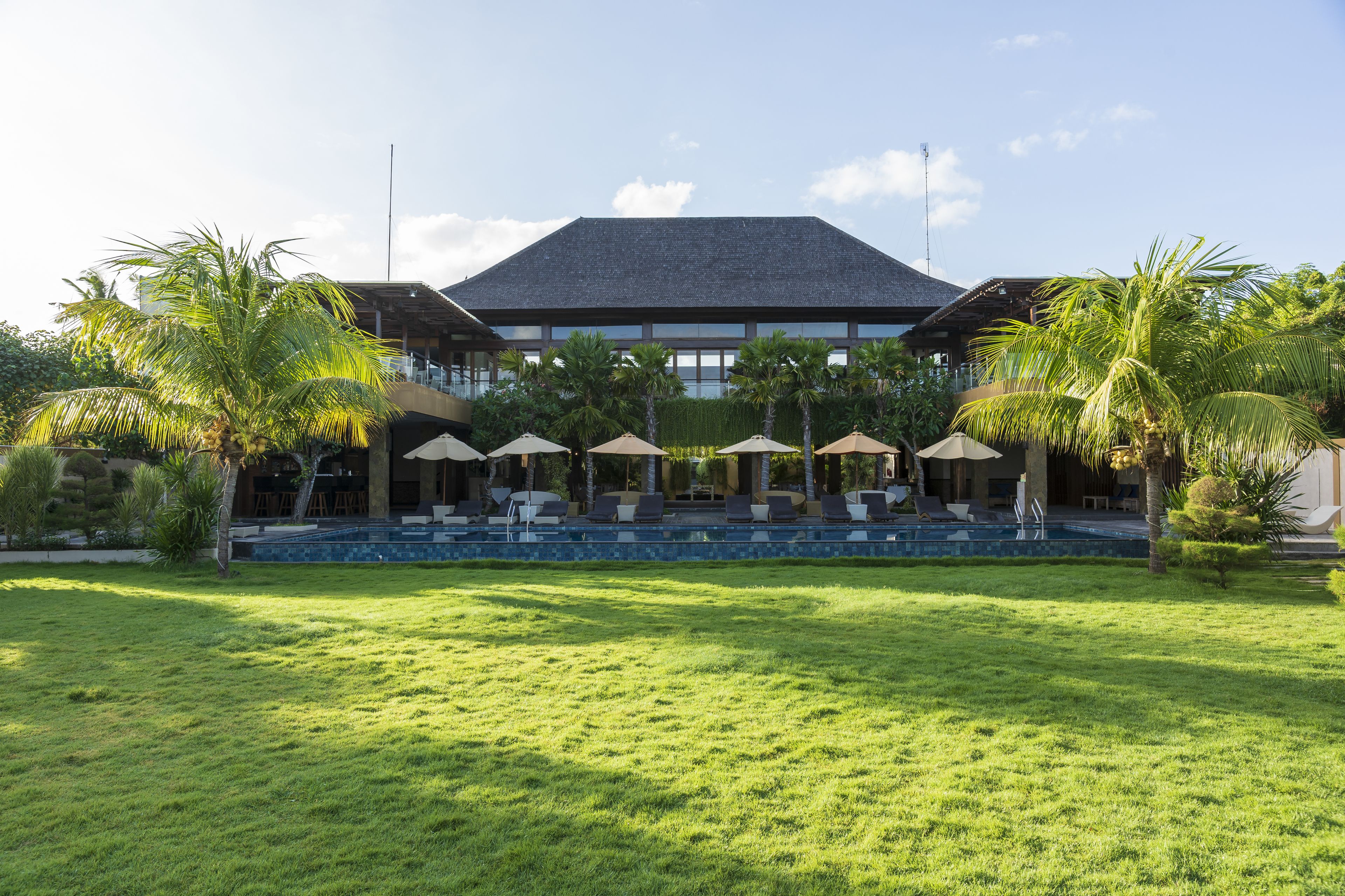 A resort with a large lawn, outdoor seating area with umbrellas, and a pool.
